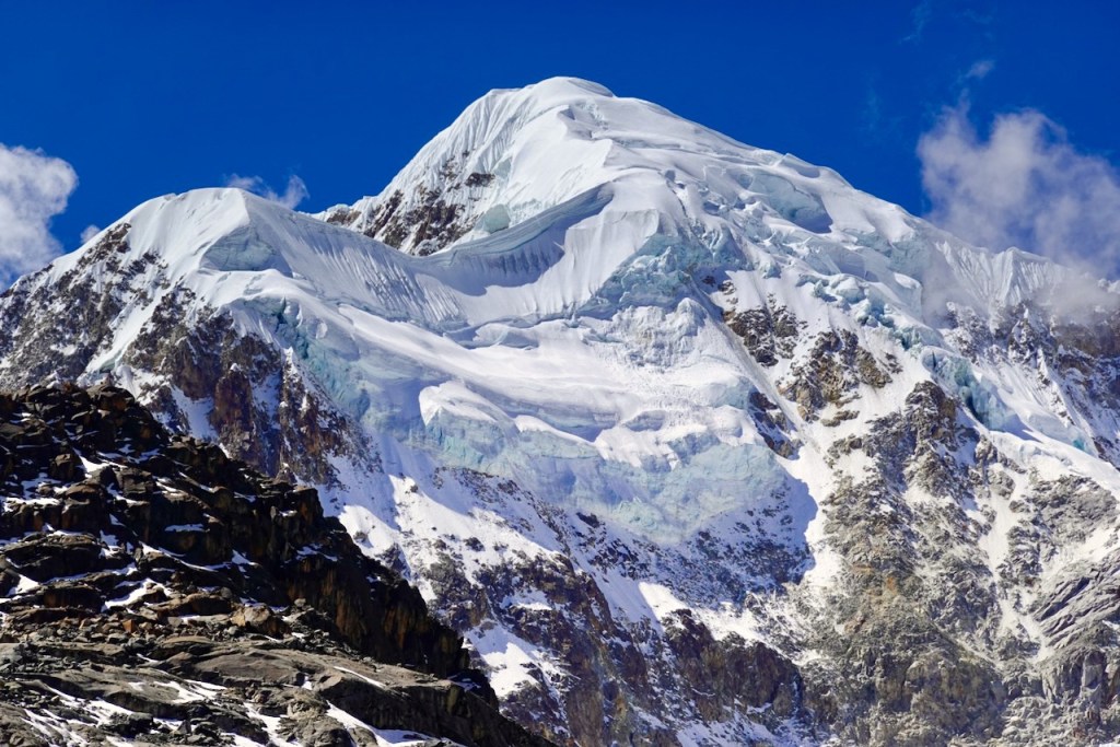 A snow-capped mountain peak with glaciers and rocky terrain under a clear blue sky.