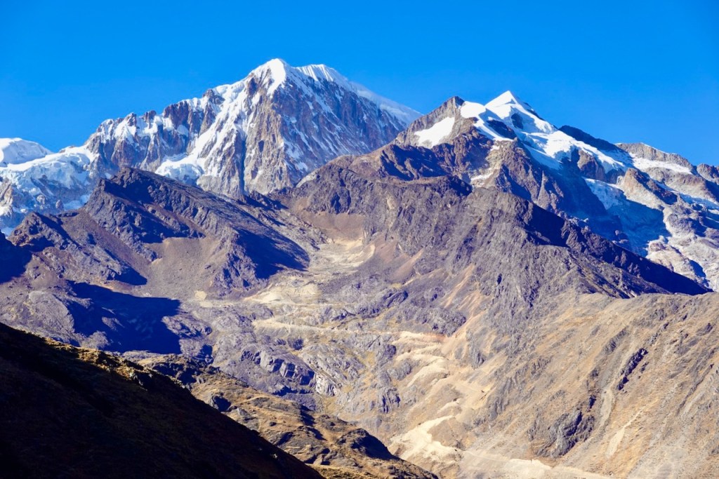 A panoramic view of rugged mountain peaks, with snow-capped summits against a clear blue sky.