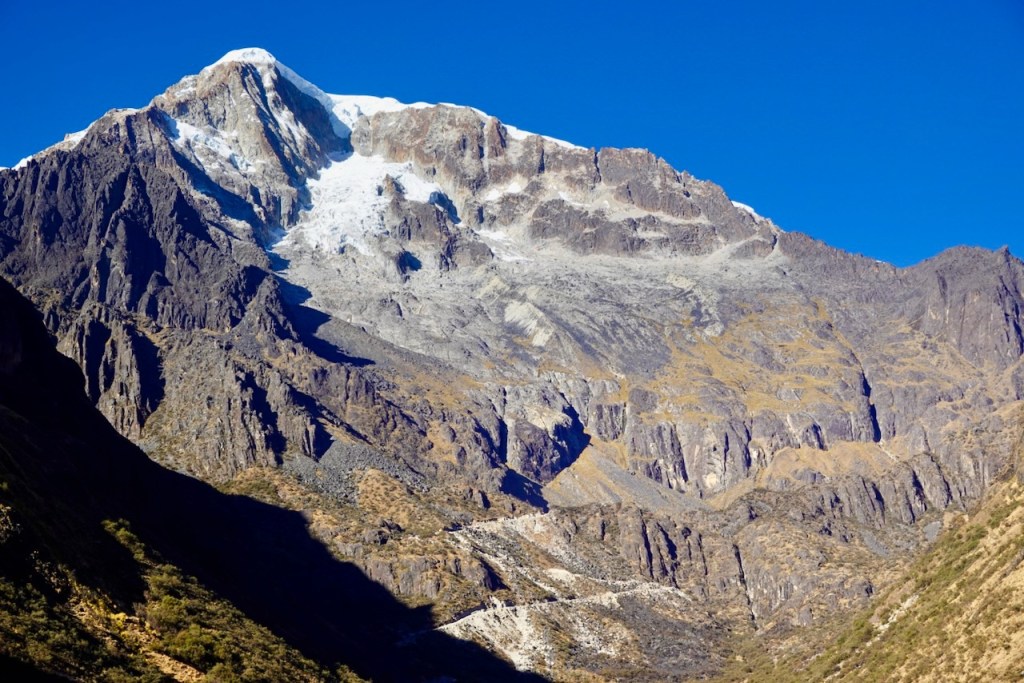Snow-capped mountain peak against a clear blue sky, surrounded by rocky slopes and valleys.