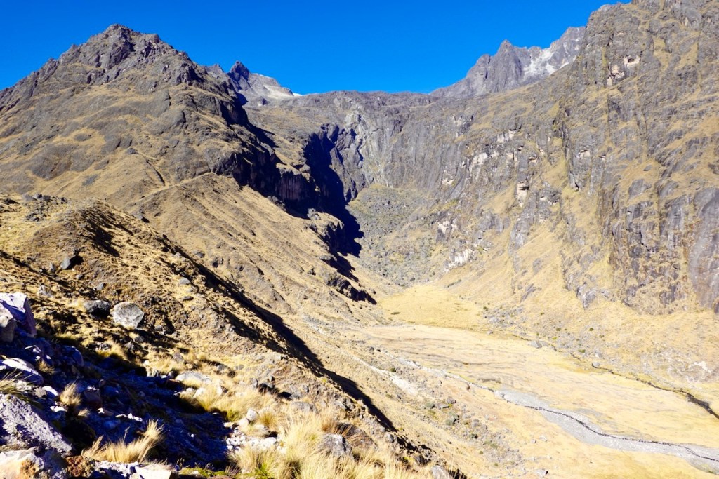 A panoramic view of a rugged mountain landscape with steep rocky cliffs and a valley below, under a clear blue sky.