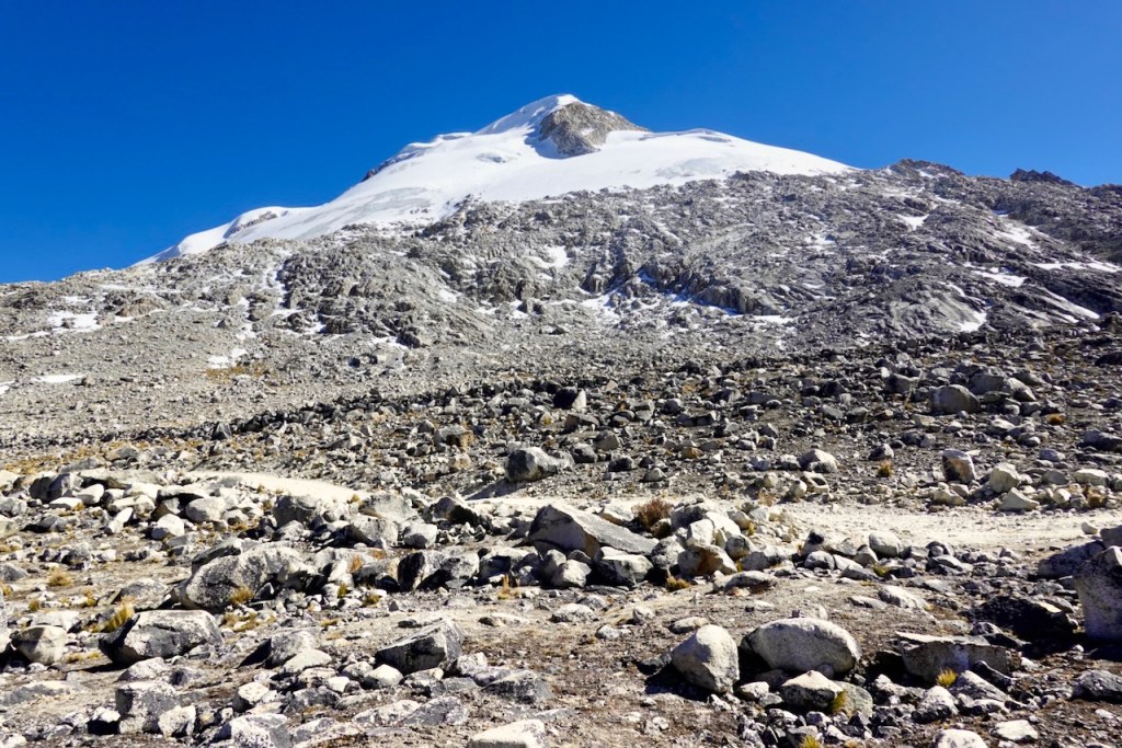 A snowy mountain peak rises above a rocky landscape under a clear blue sky.