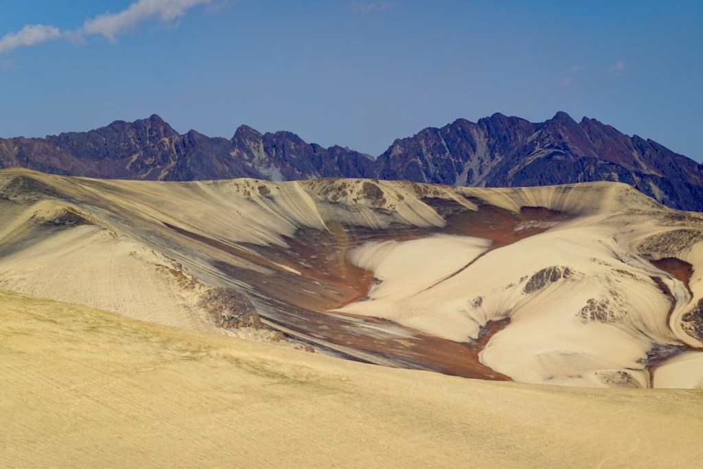 A panoramic view of rolling sandy hills and rugged mountains under a clear blue sky.