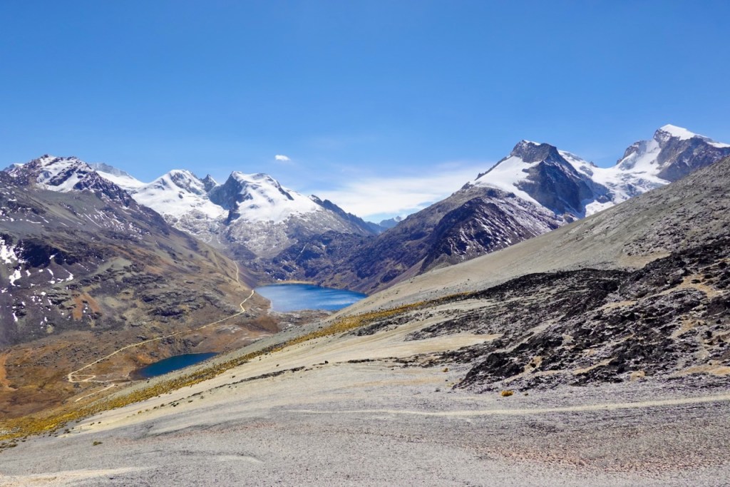 Stunning mountain landscape featuring snow-capped peaks and two glacial lakes under a clear blue sky.