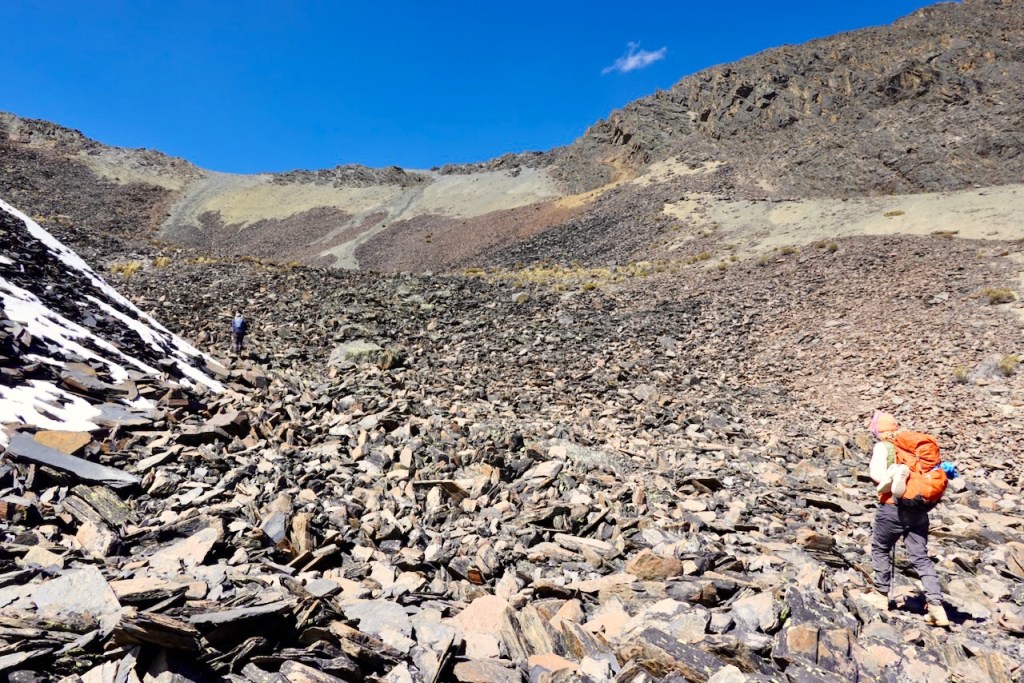 Two hikers navigating a rocky terrain under a clear blue sky.