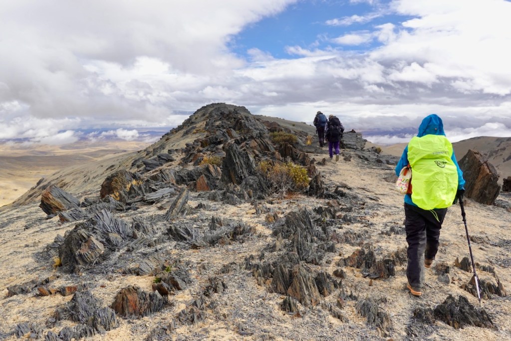 Hikers traversing a rocky mountain ridge under a cloudy sky.