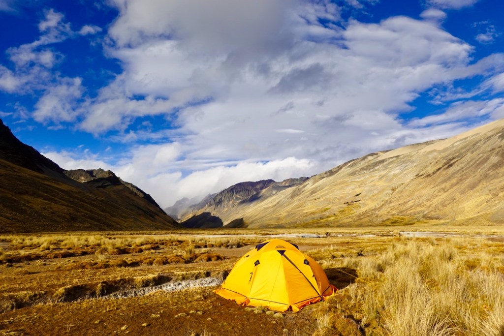A vibrant yellow tent set against a dramatic mountainous landscape under a cloudy blue sky.