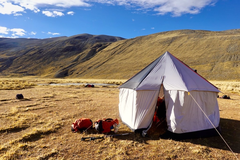 Camping tent set up on a dry, grassy plain with mountains in the background under a clear blue sky.
