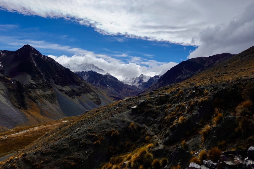 A scenic view of rugged mountains under a partly cloudy sky, with some snow-capped peaks visible in the distance.