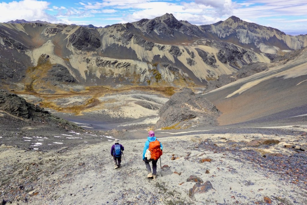 Two hikers walking down a rocky path with mountains in the background.