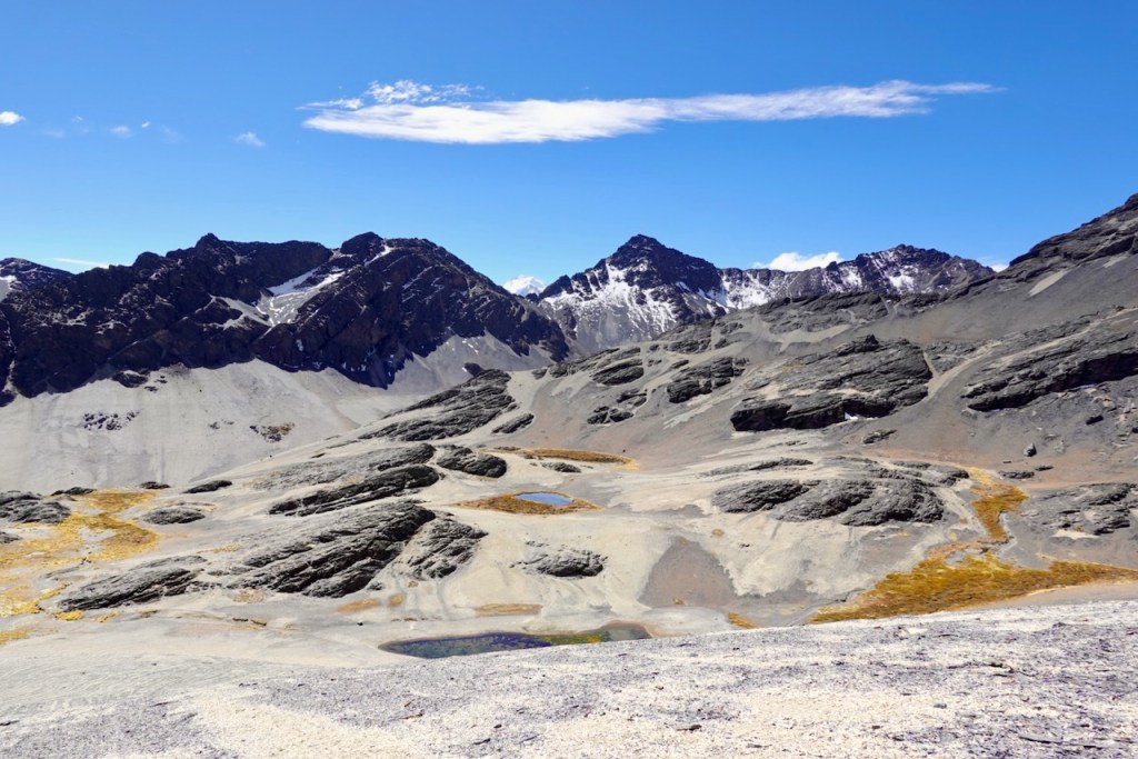 A panoramic view of rugged mountains under a clear blue sky, featuring rocky terrain and patches of grass.