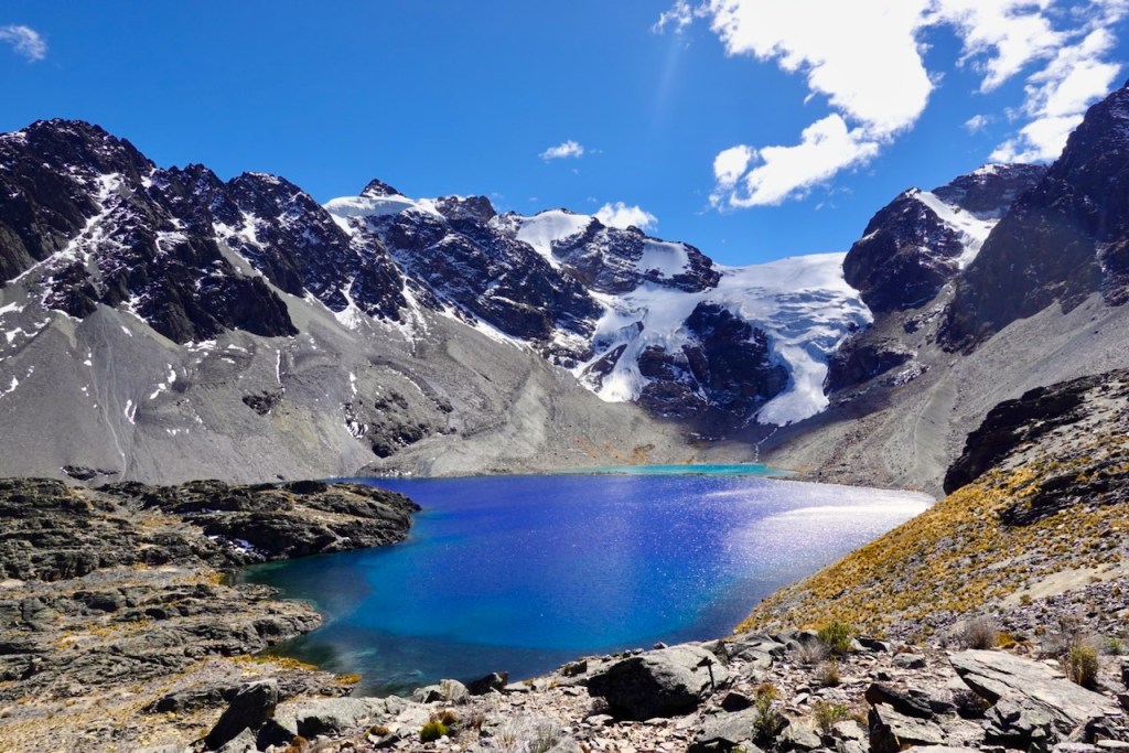 Scenic view of a turquoise alpine lake surrounded by rugged mountains and snow-capped peaks under a clear blue sky.