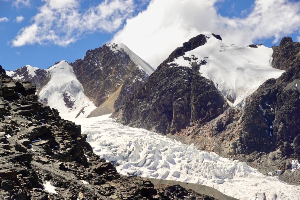 Snow-capped mountains with a glacier in the foreground under a blue sky with clouds.