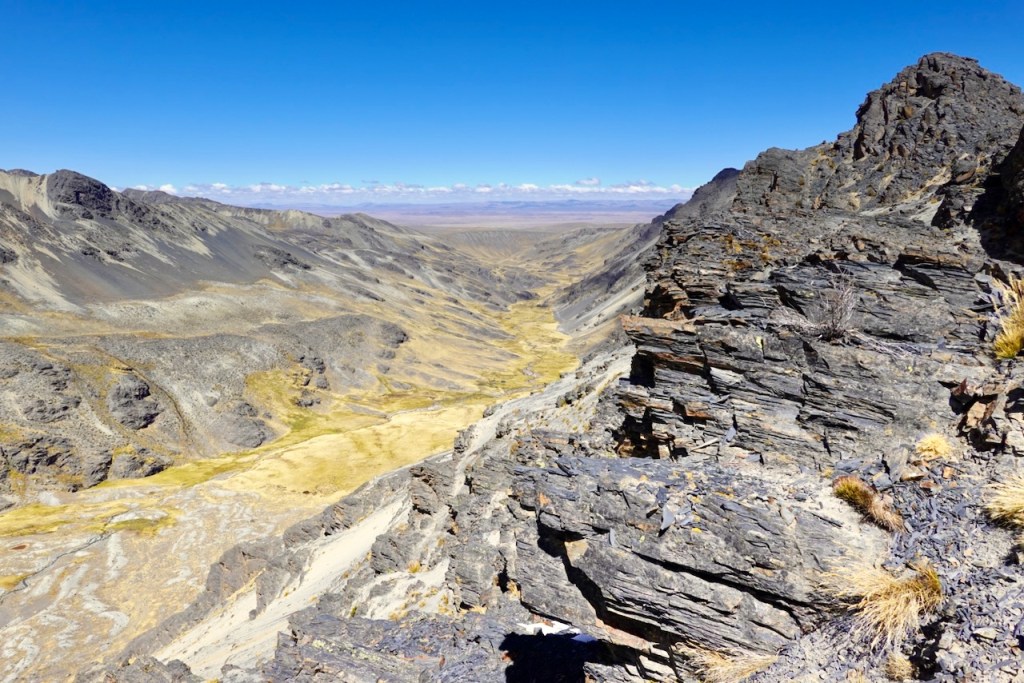 A panoramic view of a rocky mountain landscape with steep cliffs and a winding valley below, under a clear blue sky.