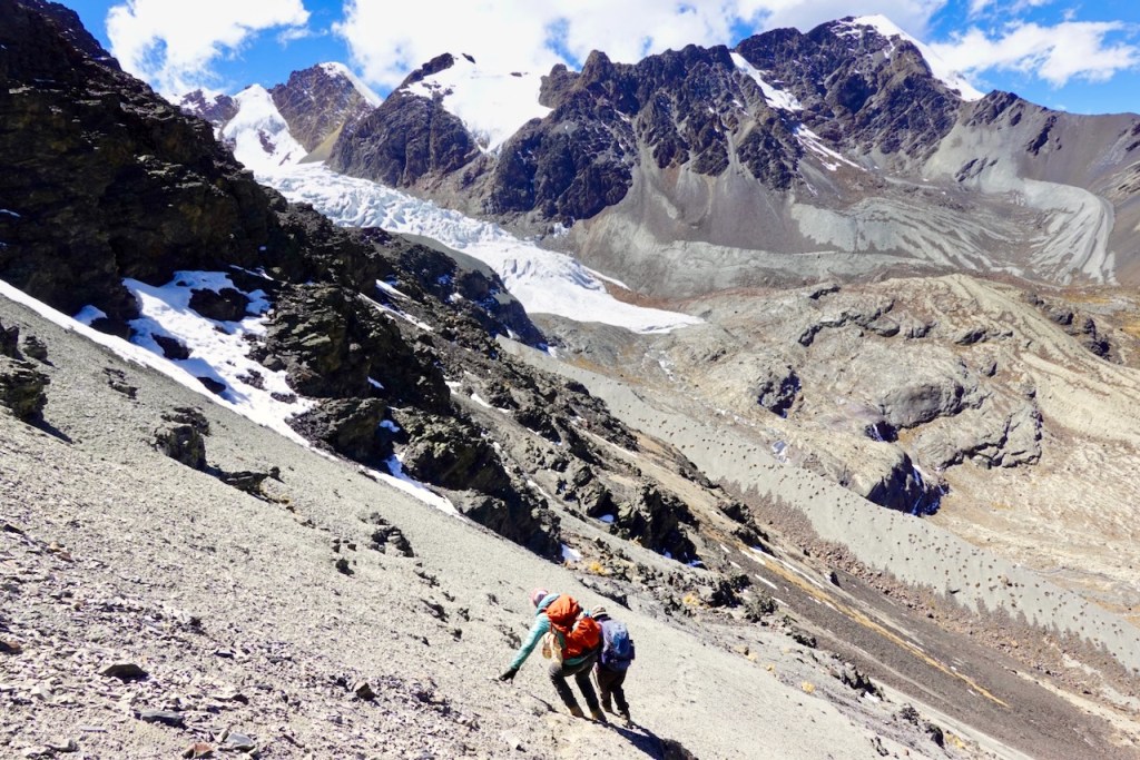 Two climbers ascending a rocky slope with snow-capped mountains in the background.
