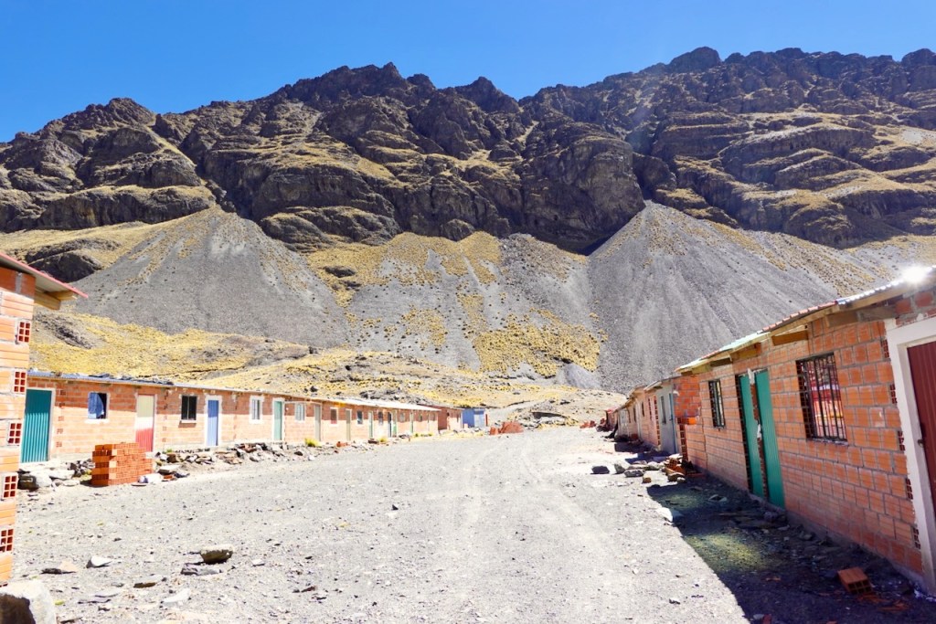 A dirt pathway lined with simple brick houses under a rocky mountain landscape.