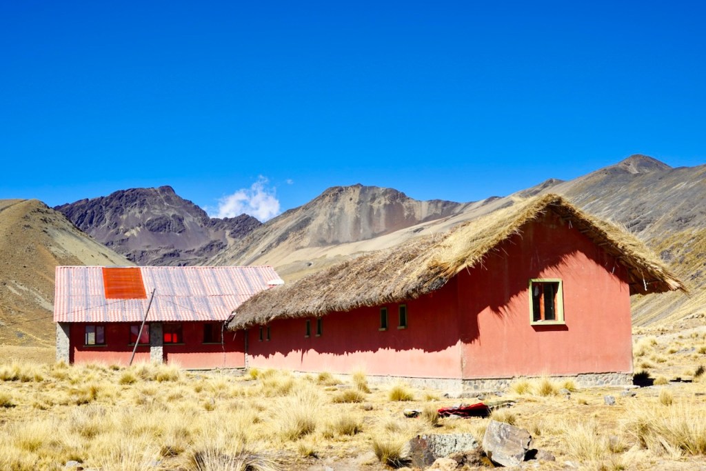 Two rustic houses with thatched roofs in a mountainous landscape under a clear blue sky.