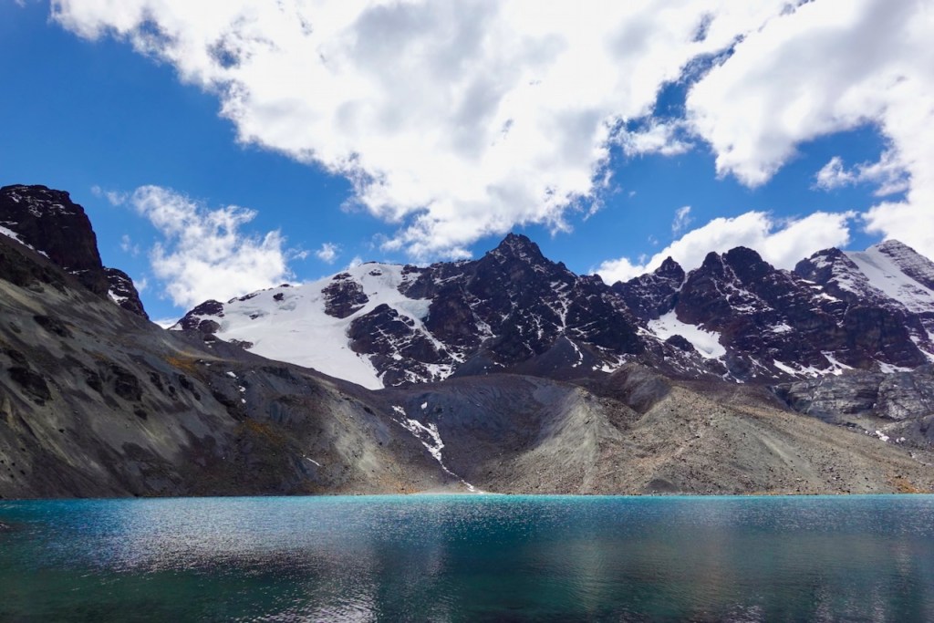 A scenic view of a turquoise lake surrounded by rocky mountains with snow-capped peaks under a partly cloudy sky.
