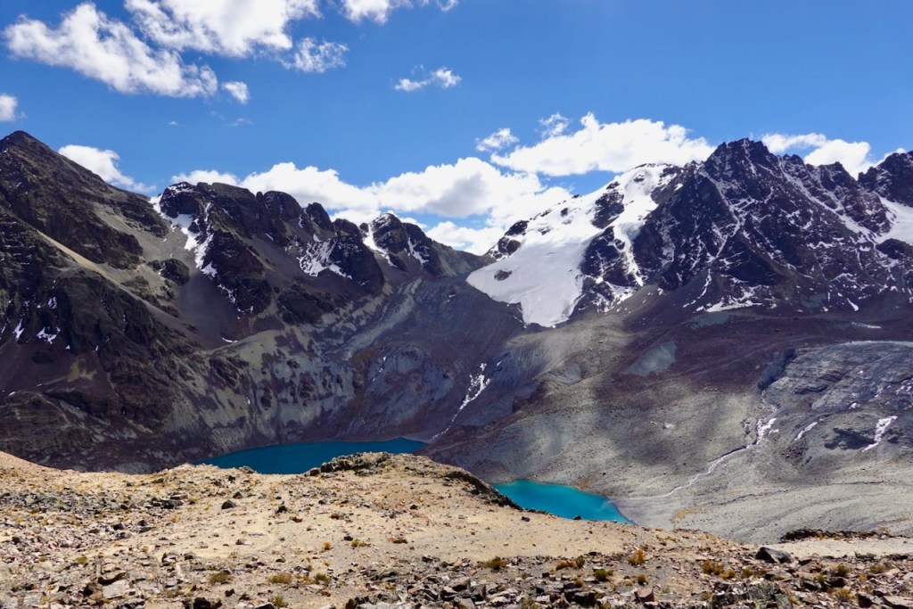 Scenic view of rugged mountains with snow-capped peaks and a turquoise lake nestled in the valley, under a partly cloudy blue sky.