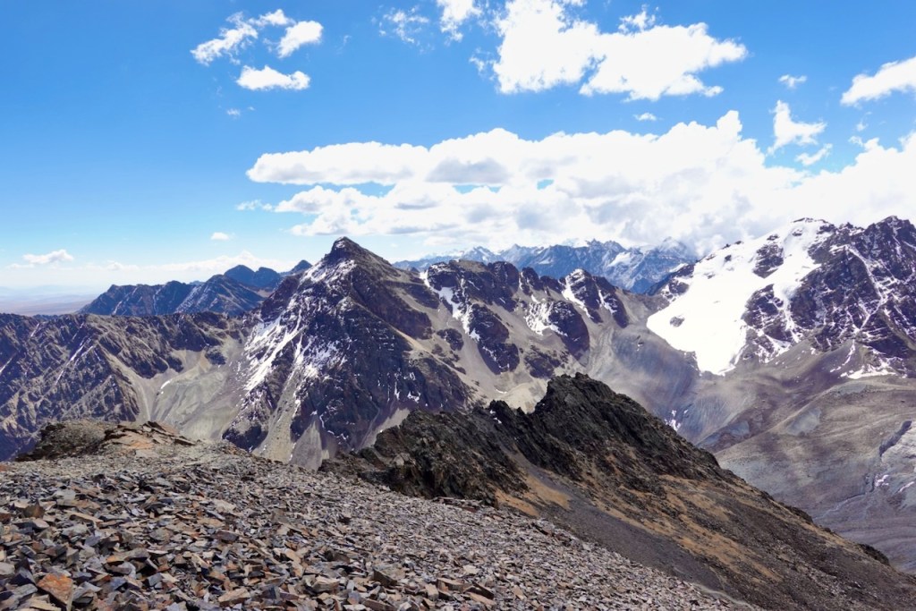 Scenic view of rugged mountains under a blue sky with scattered clouds, featuring snowy peaks and rocky slopes.