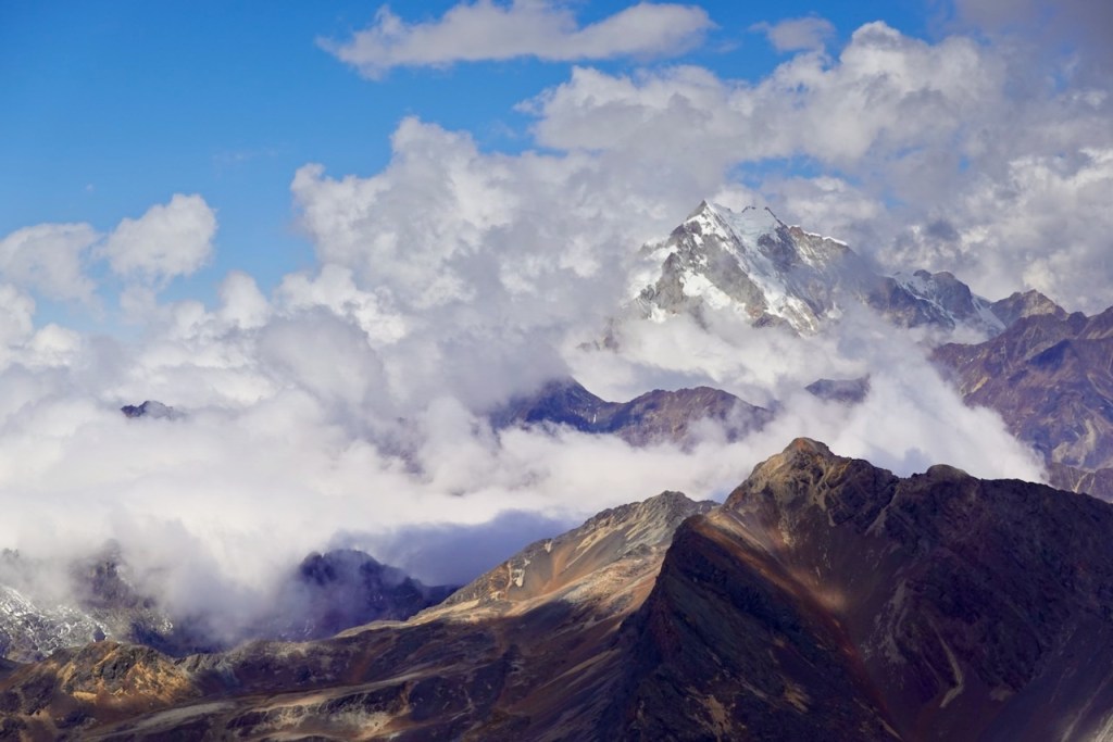 Scenic view of snow-capped mountains surrounded by clouds under a blue sky.
