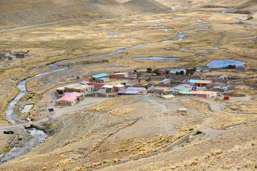 Aerial view of a small, colorful village situated in a dry, mountainous landscape with a winding river and scattered ponds.
