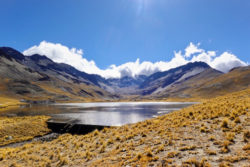 Scenic view of a serene lake surrounded by rugged mountains and bright blue sky with scattered clouds.