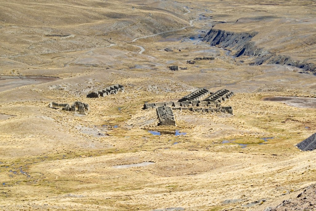 Aerial view of ancient stone ruins in a barren landscape with dry grass and sparse vegetation.