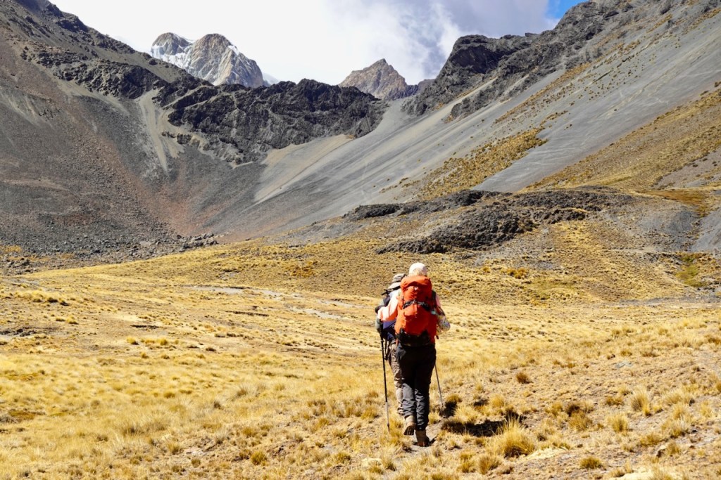 Hikers trekking through a mountainous landscape with rocky terrain and grassy patches under a cloudy sky.