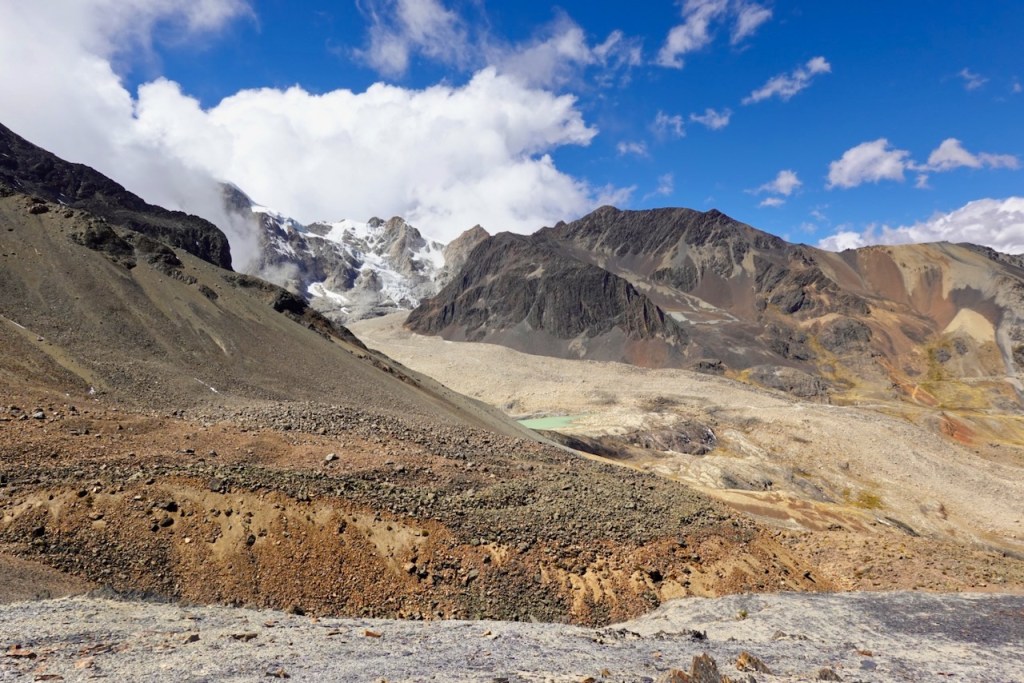 Scenic view of rugged mountain landscape with rocky slopes, snow-capped peaks, and scattered clouds under a blue sky.