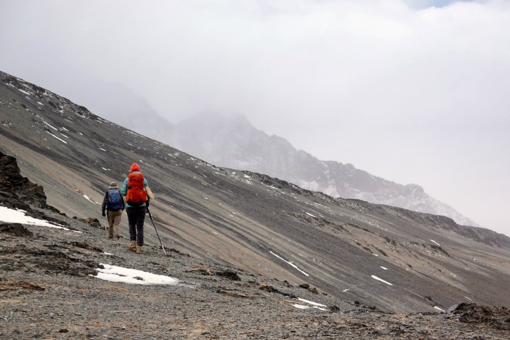 Two hikers trekking on a rocky mountain trail under a cloudy sky.